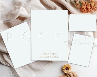 May include: Mockup of two blank white cards with the text "MOCKUP" and "PSD & JPG SMART OBJECT" on a white surface with a beige fabric and dried flowers.