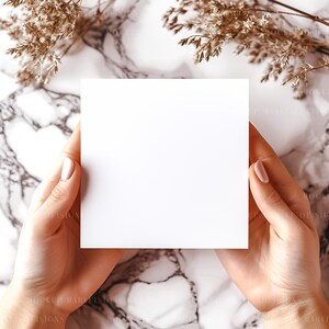 以下が含まれることがあります： 大理石の背景に、ドライフラワーを背景に、手によって持たれた空白の白いカード