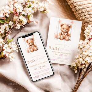May include: A baby shower invitation and a smartphone display featuring a teddy bear on a swing. The invitation and phone screen have the text "Baby Shower" and event details in pink and gold. Floral accents surround the items.