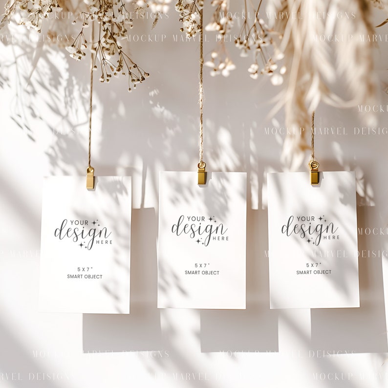 May include: Three white cards with gold clips hanging from twine against a white background. Each card has the text "Your design here" and "5x7" smart object.