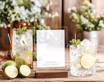 Può includere: Un cartello in acrilico trasparente con base in legno, che mostra la parola «MOCKUP». Il cartello è accanto a due bicchieri di cocktail con lime e menta, e lime freschi. Il testo «PSD & JPG SMART OBJECT» è visibile.