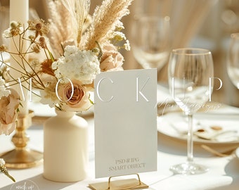 May include: A white card with the text "PSD & JPG SMART OBJECT" on a gold stand. The card is sitting on a white tablecloth with a bouquet of dried flowers in a white vase.