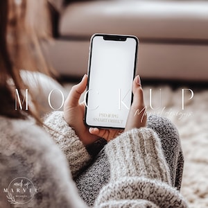 May include: A person is holding a black smartphone with a white screen. The phone is in a person's hands, and the person is wearing a grey sweater. The text "MOCKUP PSD & JPG SMART OBJECT" is on the screen.