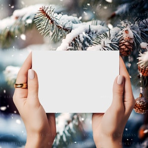 May include: A blank white card held by hands against a snowy pine tree background. The card is perfect for adding a personalized message or design.