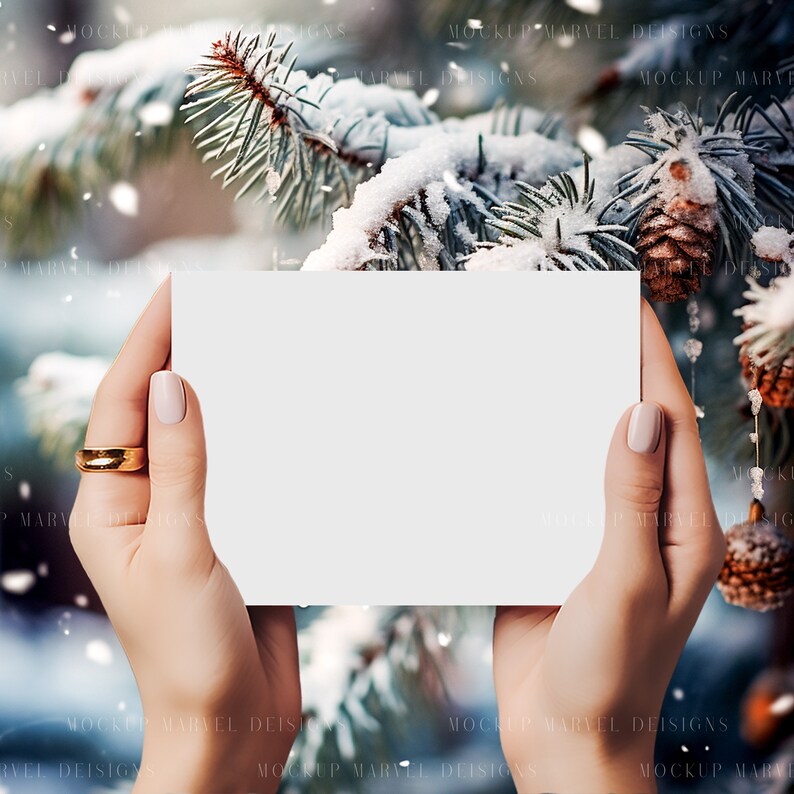 May include: A blank white card held by hands against a snowy pine tree background. The card is perfect for adding a personalized message or design.