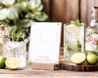 Può includere: Un'insegna trasparente in acrilico con la scritta "PSD & JPG SMART OBJECT" su una base di legno. Un cocktail rinfrescante con lime e menta è accanto all'insegna. La scena è ambientata su un tavolo di legno rustico.
