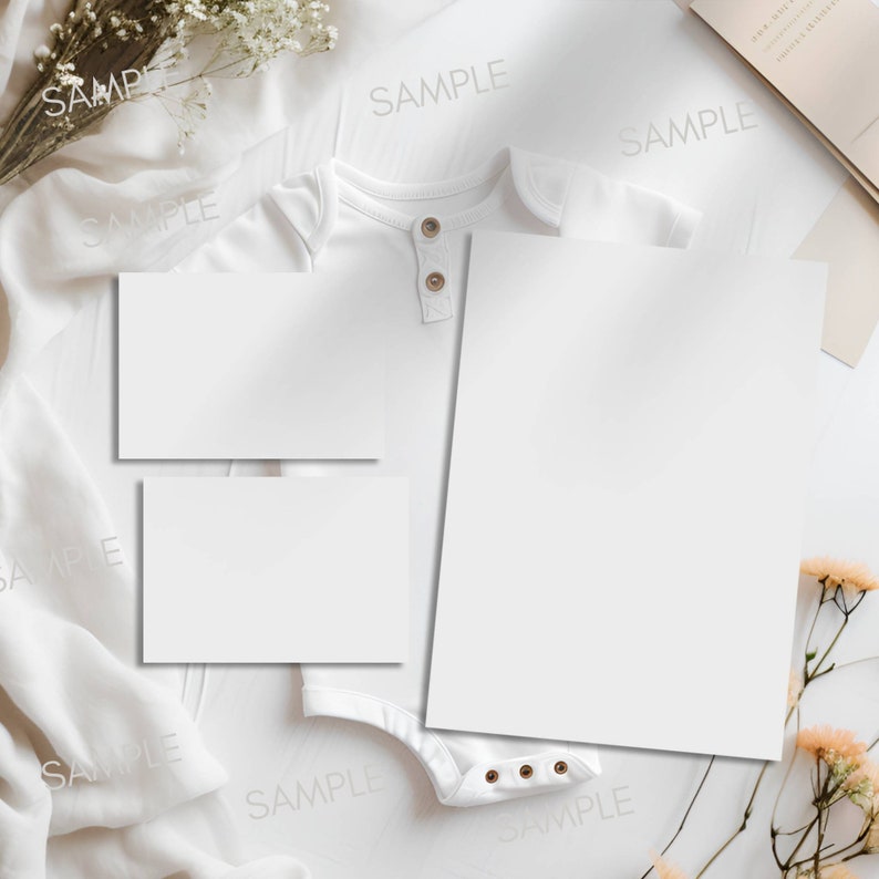 Pode incluir: Dois cart&otilde;es brancos em branco, um maior que o outro, s&atilde;o colocados sobre uma superf&iacute;cie branca. Um macac&atilde;o branco para beb&ecirc; est&aacute; sobre a superf&iacute;cie, com os cart&otilde;es cobrindo-o parcialmente. O macac&atilde;o tem um fecho de bot&atilde;o e alguns bot&otilde;es pequenos na parte inferior. A superf&iacute;cie &eacute; decorada com tecido branco e flores secas.