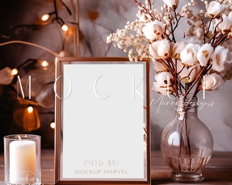 May include: A gold-toned frame with a white background sits on a wooden table. A vase with dried white flowers sits next to the frame. The text "PSD & JPG, MOCKUP MARVEL" is printed on the frame.