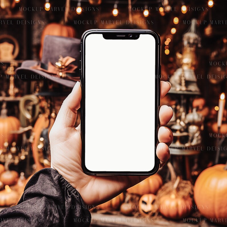 Op de afbeelding: Een hand die een zwarte smartphone met een wit scherm vasthoudt voor een Halloween-achtergrond met pompoenen, lampjes en decoraties.