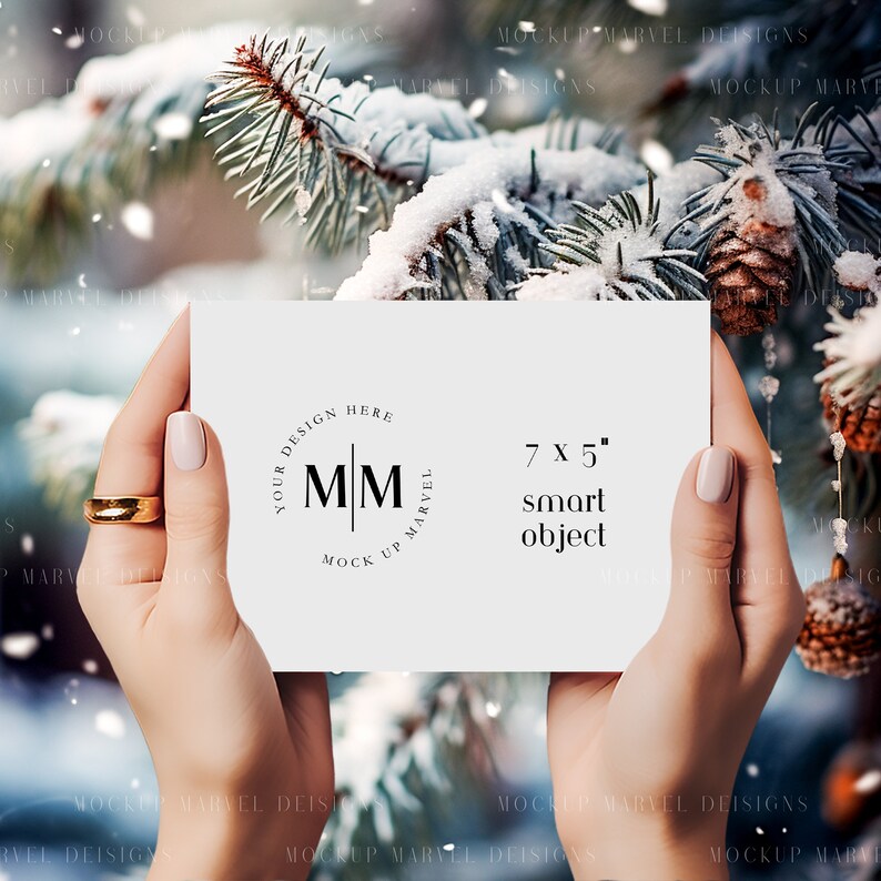 May include: A white card with a black circle logo that says "Your Design Here" and "Mock Up Marvel" with the letters "M M" in the center. The card also says "7 x 5" and "smart object". The card is being held by a person's hands against a snowy winter background.