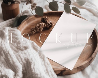 May include: A white card mockup on a wooden tray with a white blanket and dried flowers. The text "MOCKUP" and "Marvel designs" is visible on the card.