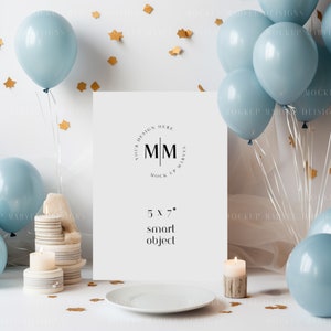 May include: A white 5x7 inch mockup frame with the text "Your Design Here" and "MM Mock Up Marvel" in a circle. The frame is on a white table with a white plate, candles, and blue balloons with gold confetti.