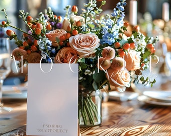 May include: A white card with the text "PSD & JPG SMART OBJECT" on a wooden stand. The card is in front of a bouquet of peach, orange, and blue flowers in a clear glass vase. The flowers are on a wooden table.