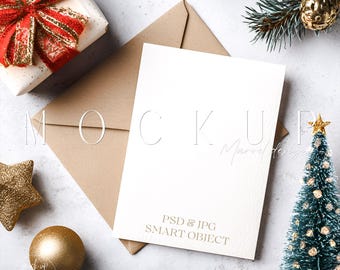 May include: A holiday-themed mockup featuring a white card with a brown envelope, a wrapped gift with a red bow, and a small Christmas tree. Gold star and ball ornaments are also present, along with text that reads "PSD & JPG SMART OBJECT".