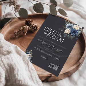 May include: A dark gray wedding invitation with white text that reads "Selena and Adam" and "Saturday 22 January 2023". The invitation features a floral design with blue and white flowers and greenery.