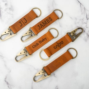 May include: Four brown leather keychains with metal clasps and rings. The keychains are engraved with the names "JJ", "JAMES", "Ooh Baby", and "SR".