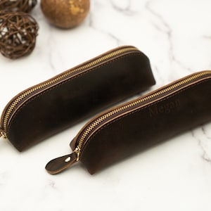 May include: Two brown leather pencil cases with gold zippers. One case has the name "Megan" embossed on it.