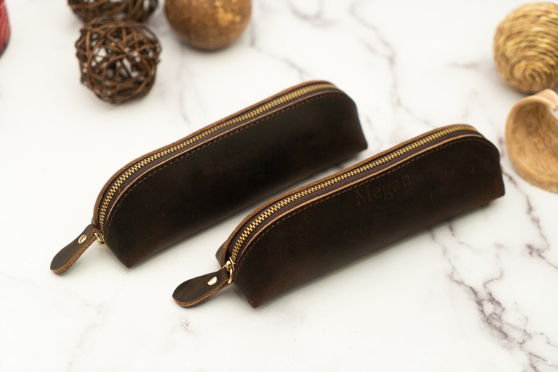 May include: Two brown leather pencil cases with gold zippers. One case has the name "Megan" embossed on it.
