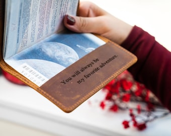 May include: A brown leather passport holder with the text "You will always be my favorite adventure." engraved on the front.