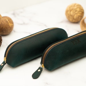May include: Two green leather pencil cases with gold zippers. The smaller case has the initials "YSK" embossed on the front.