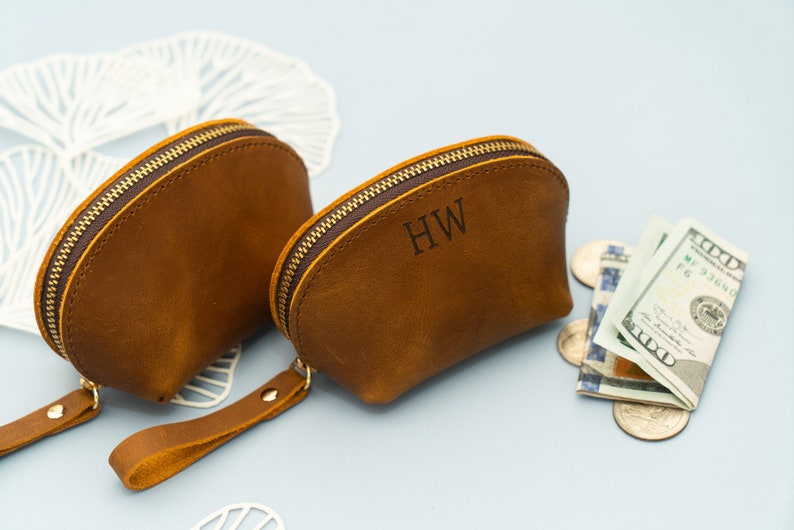 May include: Two brown leather coin purses with zipper closures and a strap. The purse on the right has the initials "HW" engraved on the front.