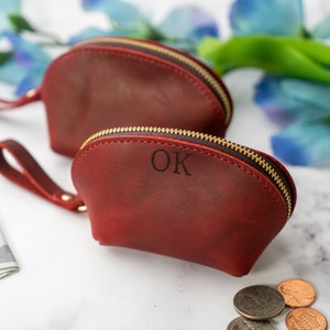 May include: Two red leather zippered pouches with gold zips. The smaller pouch has the initials "OK" embossed on the front.