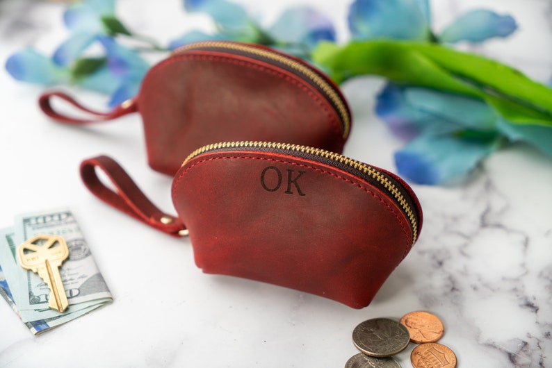 May include: Two red leather zippered pouches with gold zips. The smaller pouch has the initials "OK" embossed on the front.