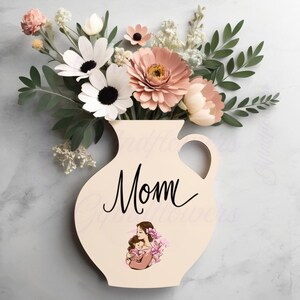 May include: A cream-colored vase-shaped wooden sign with the word "Mom" in elegant script. The vase holds paper flowers in shades of pink, white, and green. A small illustration of a mother and child is at the bottom.