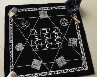 May include: Black cloth with white lines forming a grid pattern with symbols and numbers. The cloth is surrounded by a white border with numbers and symbols. There are small stones and a matchstick on the cloth.