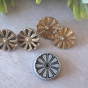 May include: A collection of decorative cabinet knobs in various finishes. The knobs feature a radial design with a central circular element. The knobs are in shades of gold and silver, with a detailed, textured appearance. The knobs are likely made of metal.