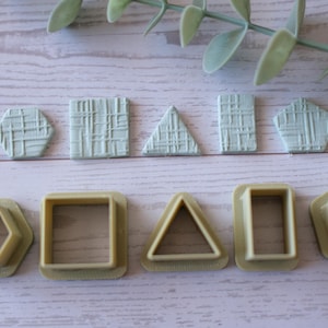 Op de afbeelding: Een verzameling geometrisch gevormde koekjessnijders in verschillende vormen, waaronder een zeshoek, een vierkant, een driehoek en een vijfhoek. De snijders zijn lichtgeel en de vormen zijn ook weergegeven in een getextureerd, lichtgroen materiaal.