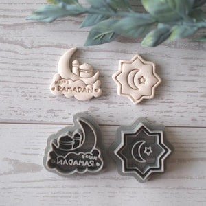 May include: Four cookie cutters with Islamic designs. Two are beige, one with a crescent moon and mosque, the other with a star and crescent. The other two are gray, with the same designs. One says "Happy Ramadan".