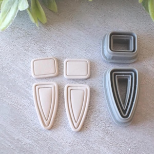 May include: An assortment of polymer clay cutters in various shapes. The cutters include two rectangular shapes, two teardrop shapes, and two square shapes. The cutters are in shades of gray and beige.
