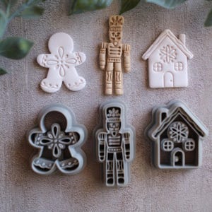 May include: A selection of Christmas cookie cutters. The image shows a gingerbread man, a nutcracker, and a house, presented as both cut-out shapes and finished cookies. The colour palette is muted, highlighting the shapes and intricate details.