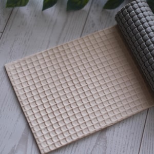 May include: A beige and gray textured yoga mat, partially rolled up, rests on a light wood-grain surface. The mat's surface has a waffle-like pattern. The rolled portion is gray, and the unrolled section is beige.