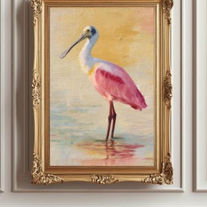 May include: An oil painting of a roseate spoonbill bird in a gold ornate frame. The bird has pink feathers and stands in shallow water. The background is a blend of yellow, pink, and blue hues.