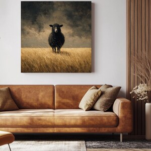 K&ouml;nnte beinhalten: Gerahmter Leinwanddruck mit einem schwarzen Schaf, das in einem Feld aus goldenem Gras unter einem st&uuml;rmischen Himmel steht. Das Kunstwerk h&auml;ngt &uuml;ber einem braunen Ledersofa mit Kissen.