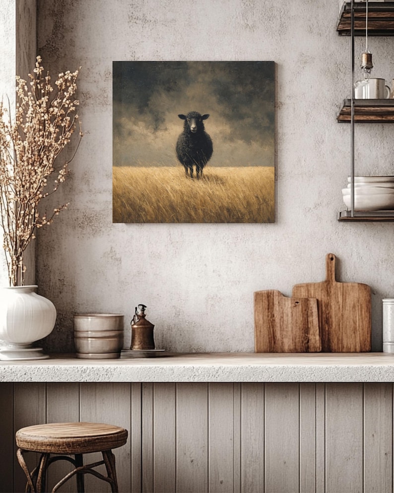 K&ouml;nnte beinhalten: Quadratische Leinwandkunst mit einem schwarzen Schaf, das in einem Feld aus hohem, goldenem Gras unter einem bew&ouml;lkten Himmel steht. Das Kunstwerk hat eine Vintage- und rustikale &Auml;sthetik, passend f&uuml;r Bauernhaus- oder Landhausdekoration.