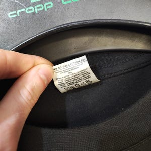 May include: A black t-shirt with a tag visible. The tag includes the text "ww.BC-COLLECTION.EU" and washing instructions. The shirt is hanging on a black hanger with the green text "cropp town".