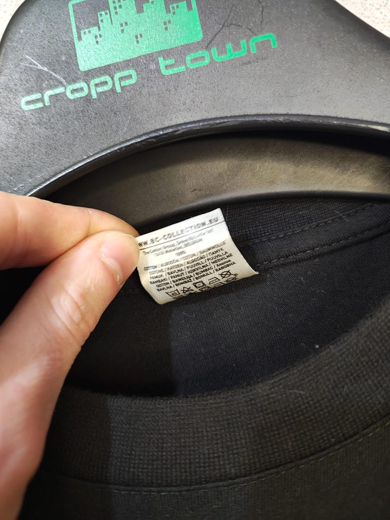May include: A black t-shirt with a tag visible. The tag includes the text "ww.BC-COLLECTION.EU" and washing instructions. The shirt is hanging on a black hanger with the green text "cropp town".