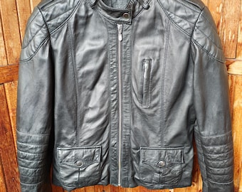 May include: Black leather jacket with a stand-up collar, a front zipper, and two front pockets with button closures. The jacket has quilted shoulder and sleeve details. The jacket is hanging on a black hanger.