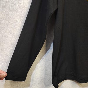 May include: Black long-sleeve shirt with a yellow design on the shoulder. The shirt is made of a soft material and has a crew neck. The sleeve is visible on the left side of the image.