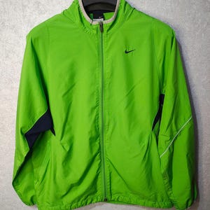 May include: Bright green Nike zip-up jacket with a small black logo on the chest. The jacket has a full zipper, a light gray collar, and navy blue accents on the sides. A white stripe runs down the sleeves.