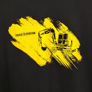 May include: Black sweatshirt featuring a yellow excavator graphic with the text "PROUD TO PERFORM" on a yellow brushstroke design. The excavator is a detailed illustration of heavy machinery.