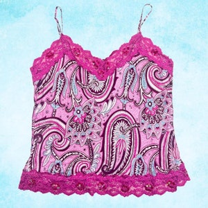 Puede incluir: Un camisón rosa con un estampado de cachemira en tonos rosa, blanco y azul. La parte superior presenta un ribete de encaje festoneado en un color rosa más oscuro a lo largo del escote y el dobladillo, con finas correas de espagueti.