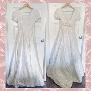 Puede incluir: Dos vestidos de novia color marfil colgados de perchas de madera. Los vestidos tienen mangas cortas y un escote cuadrado. Un vestido presenta detalles de encaje en el corpiño y las mangas. El otro vestido tiene adornos florales en la cintura.