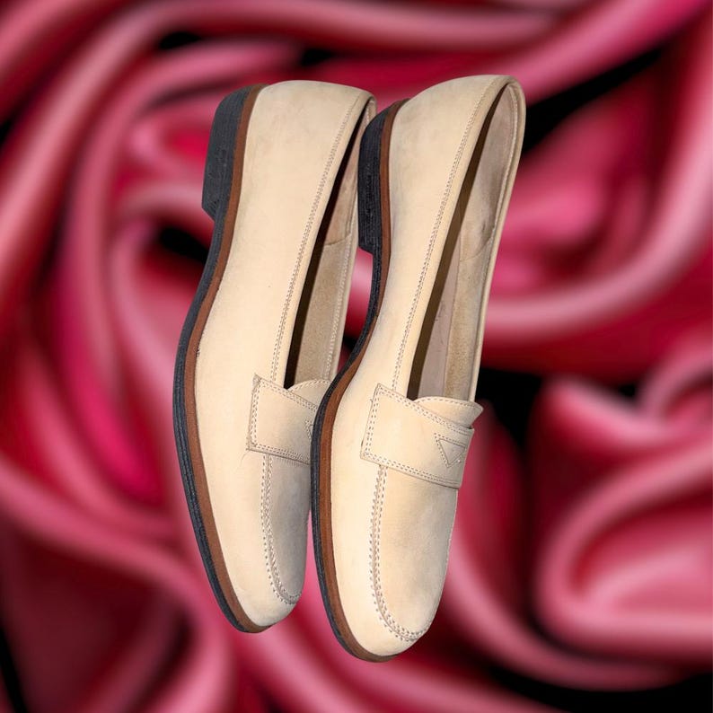 Puede incluir: Un par de mocasines de cuero beige con un dise&ntilde;o cl&aacute;sico. Los zapatos tienen una puntera redondeada, una correa de centavo y una suela marr&oacute;n oscuro. Las costuras son visibles y los zapatos parecen nuevos.