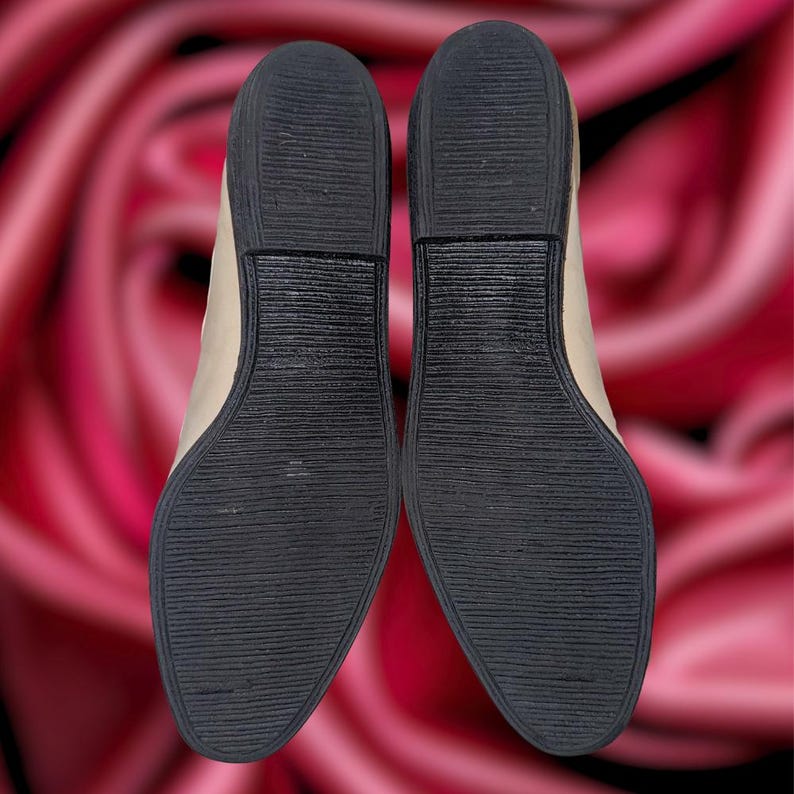 Puede incluir: Un par de zapatos de tac&oacute;n cu&ntilde;a beige con suelas de goma negras. Las suelas tienen un patr&oacute;n texturizado y acanalado para el agarre. Los zapatos se muestran sobre un fondo borroso de tonos rojos y rosas, que se asemeja a una rosa.