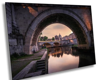 Könnte beinhalten: Blick auf eine Steinbogenbrücke über einen Fluss in Rom, Italien. Die Brücke wird vom untergehenden Sonnenlicht beleuchtet, und die Skyline der Stadt ist in der Ferne sichtbar.