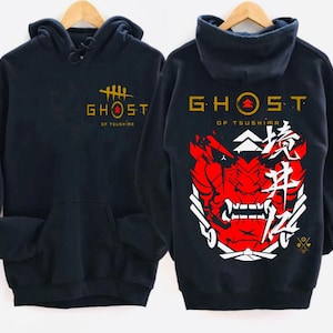 May include: Black hooded sweatshirt with a gold "Ghost of Tsushima" logo on the front and a red and white samurai mask with Japanese characters on the back.